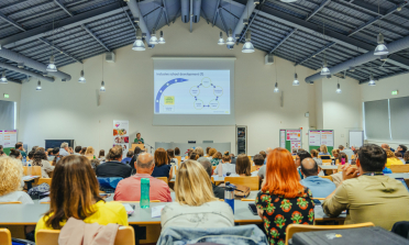 People listening to a presentation in a large room with a screen at the front