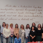 A group of people stand in front of a white wall with text written on it in Hungarian