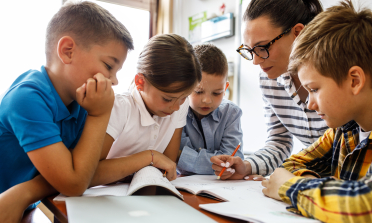Four children sit with their teacher and read their work